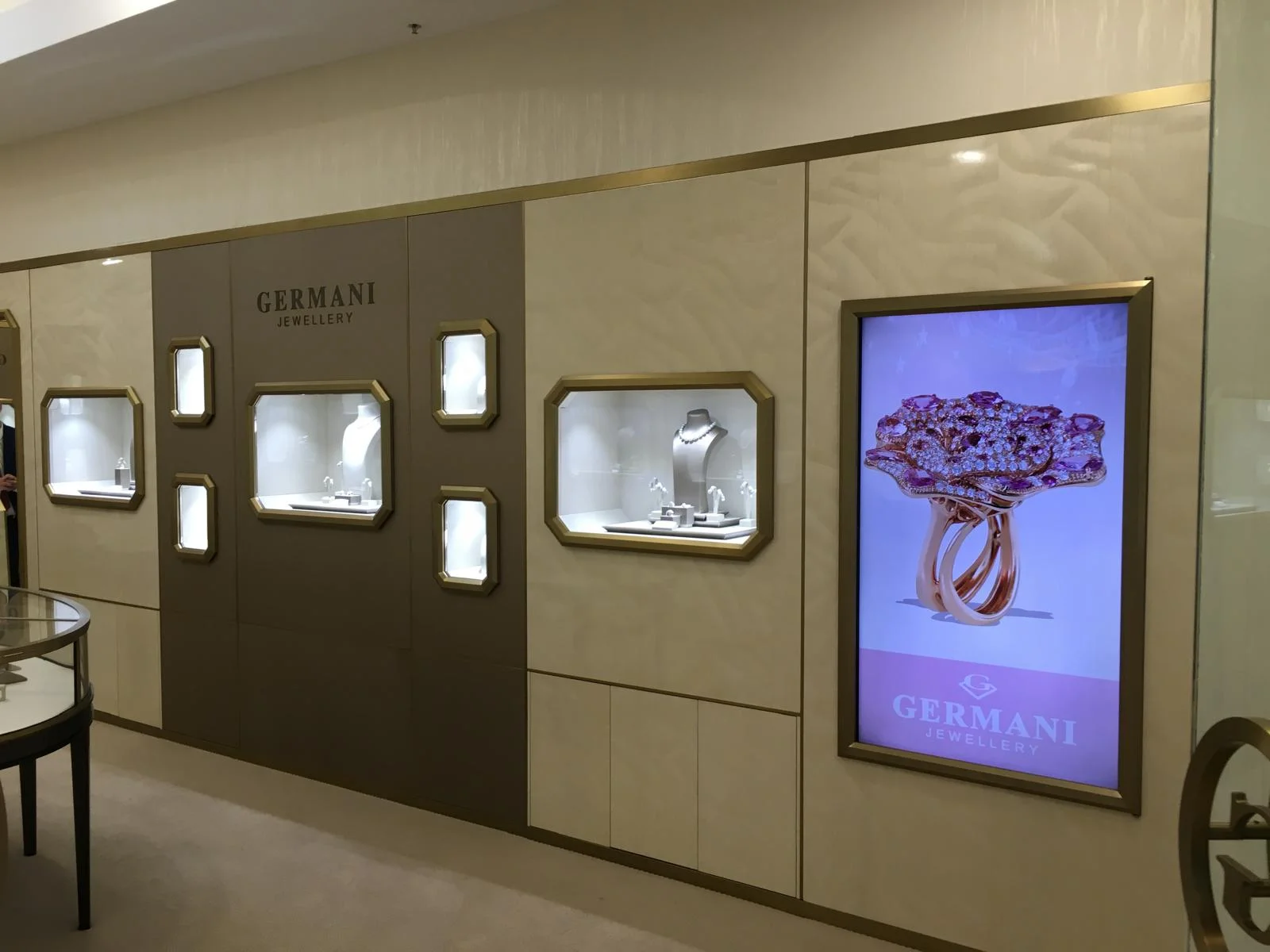 A Germani boutique wall of gold-framed display windows beside a screen showing a rose-gold flower ring