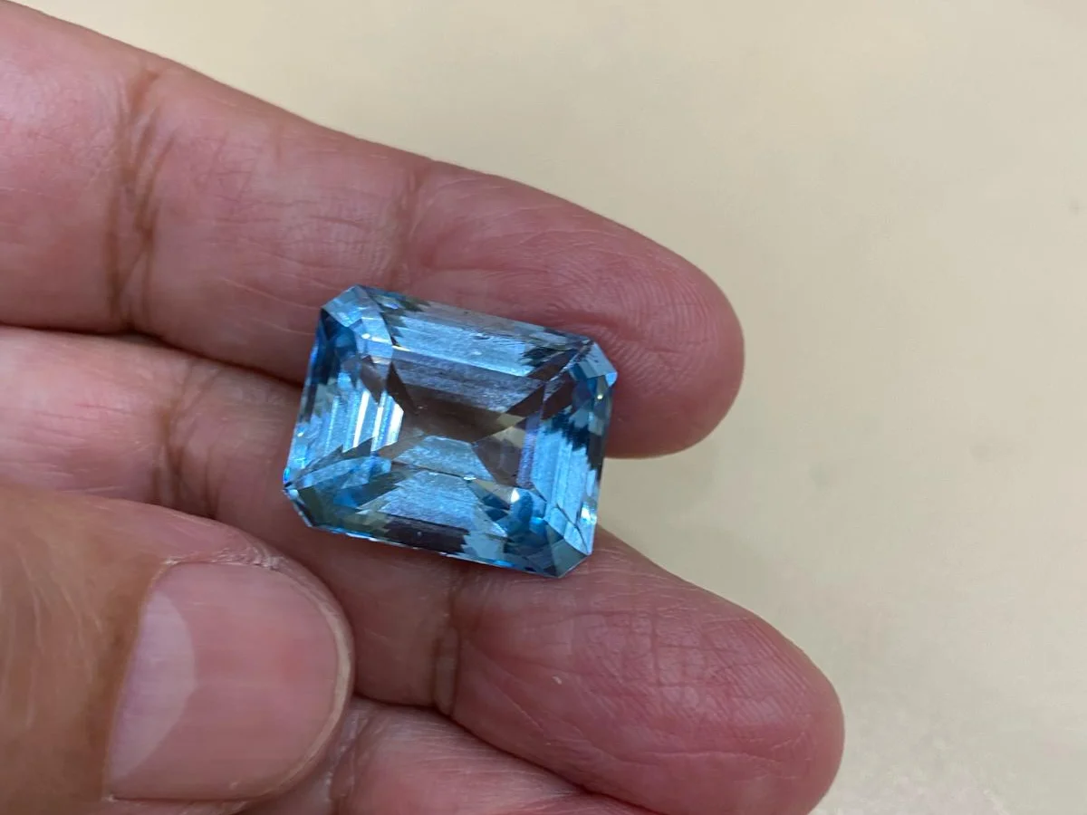 A large emerald-cut aquamarine held in the hand for inspection