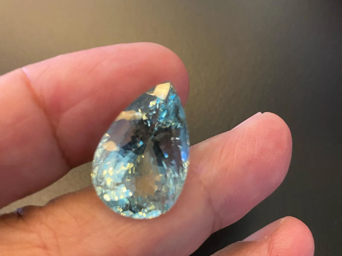 A large pear-shaped aquamarine held between the fingers for inspection